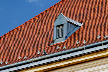 Sloped red clay tile roof . round ridge tiles. gray Zink plated roof dormer of metal louver vent....