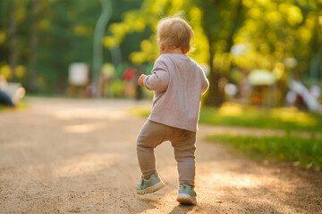 Rear view as a little child baby in the park in the summer on the setting sun walking along the path