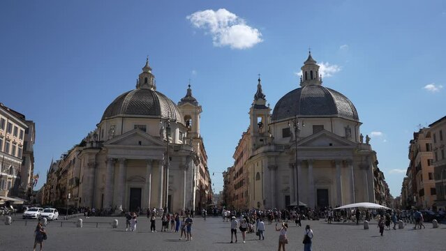 Rome, Italy - 5 September 2023. Pair of basilicas for Santa Maria in Montesanto and Santa Maria dei Miracoli in Piazza del Popolo with people walking around, on sunny day with blue sky on background.