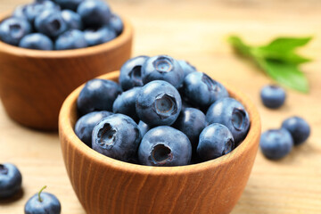 Bowls of fresh tasty blueberries on wooden table, closeup
