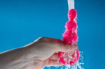Woman holding pink anal beads under running water on blue background. Sex toy hygiene concept.