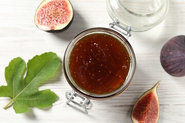 Glass jar with tasty sweet jam, green leaf and fresh figs on white wooden table, flat lay