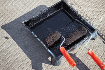 Paint roller in tray with black industrial paint or primer. Top view of paint roller with paint...