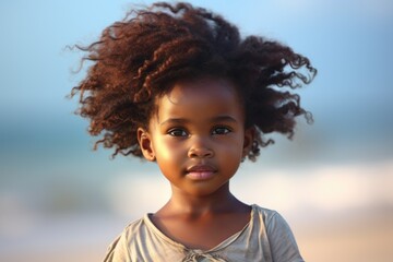 A little girl standing on a beach next to the ocean. This image can be used to depict a relaxing vacation, a family outing, or a summer adventure.