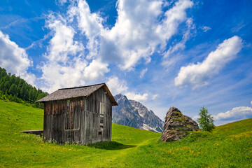 Idyllic alpine wooden farm house scenery in Italian dolomites with view on Rotwand mountain and  colorful green meadows, sunny day, blue sky