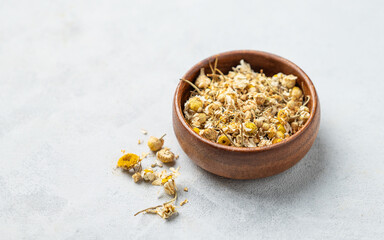 Dried chamomile in a wooden bowl on a light background. Healthy food and drink concept. Herbal  and alternative medicine with dry herbs.