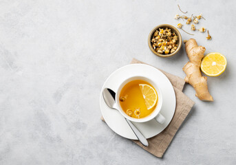 Chamomile herbal tea with lemon in a white cup on a light background with dry flowers and ginger....