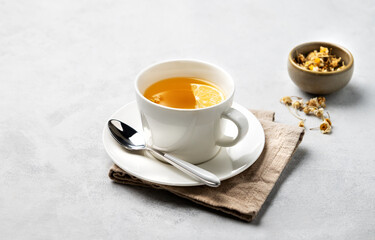 Chamomile herbal tea with lemon in a white cup on a light background with dry flowers. The concept of a healthy detox drink for health and sleep.