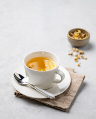 Chamomile herbal tea with lemon in a white cup on a light background with dry flowers. The concept of a healthy detox drink for health and sleep.