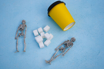 Refined sugar chunks are lying on a blue table, next to two skeletons, the concept of unhealthy...