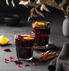 Mulled wine with orange, apple, pomegranate and cinnamon in glasses on a dark background. The concept of a traditional winter hot drink with spices and fruits