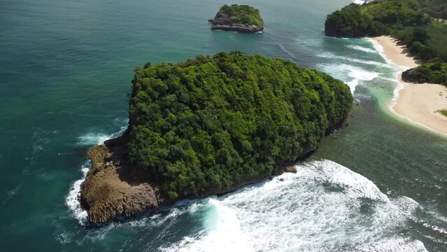 Orbital Aerial view of a small island covered with tropical trees at Tanjung Penyu Mas Beach