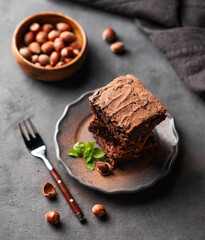 A stack of chocolate brownies with mint and  hazelnuts on a dark  background with nuts. The concept of vegetarian and sweet homemade baked goods.