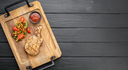 Top view of pork steak served on a wooden board in a restaurant on a dark background