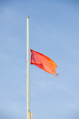 Red rag flag prohibiting swimming against the sky.