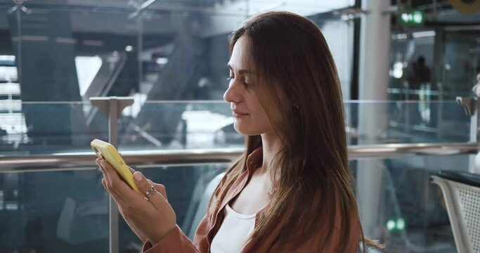Airport terminal. beautiful smiling woman holds smartphone checking flight getaway concept. woman standing right on the background of the airport and texting message. Female tourist wants getaway