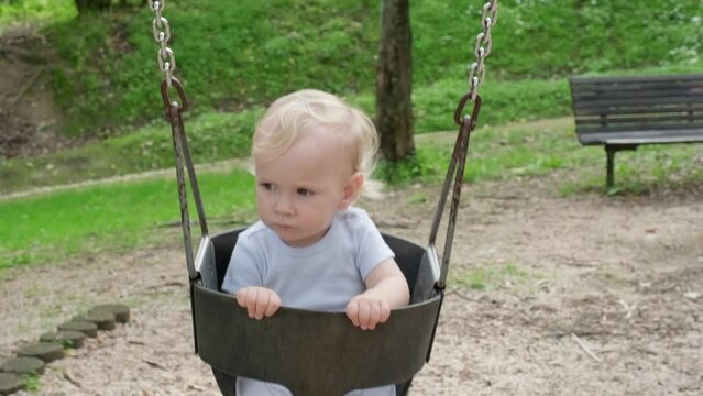 Small caucasian Child having fun swinging on a swing on the kid's playground. Beautiful kid swinging on a swing and smiling on a nice summer day in the park. Slow motion.