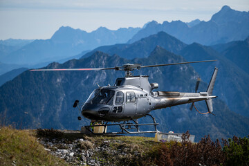Gray cargo helicopter lands on ridge of a mountain in the Alps in autumn