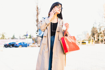 Happy tourist woman with shopping bags walks through the sunny streets of Europe. Beautiful woman enjoys the weather after shopping. Consumerism, shopping. Active lifestyle