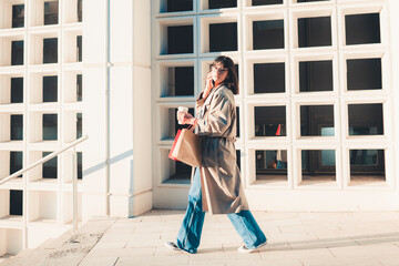 Happy tourist woman with shopping bags walks through the sunny streets of Europe. Beautiful woman enjoys the weather after shopping. Consumerism, shopping. Active lifestyle