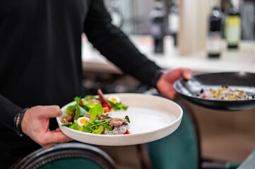 chef or waiter hold plate with Salad nicoise. Tuna, with green beans, tomatoes, potatoes and a vinaigrette mustard dressing