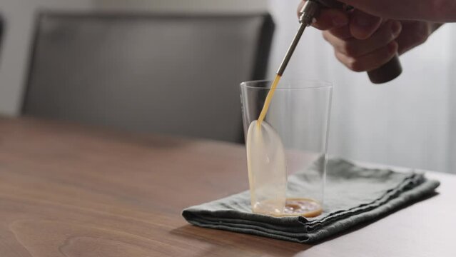Slow motion making nitro coffee in thin glass on walnut table