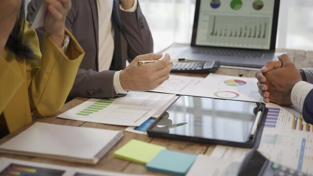 Group of modern Asian young businessmen in suits are brainstorming while sitting in a business meeting. Planning, strategy, new business development with graph documents and laptops.