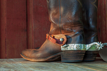 Old brown cowboy boots with spurs on a wood surface in sunlight - obrazy, fototapety, plakaty