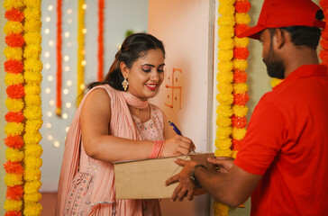 Happy girl receiving delivery box from delivery boy by signing on papers during Diwali festival day - concept of festive ecommerce order, fast delivery service and online shopping