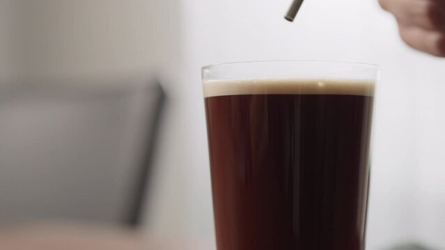 Slow motion making nitro coffee in thin glass on walnut table