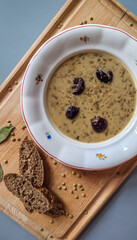 Brown lentil soup with cream and prunes is a traditional Christmas, New Year's soup in Slovakia. Healthy vegetarian dish on a vintage white plate with ornaments and bread slices on the cutting board. 
