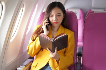 Asian woman sitting on airplane playing with cell phone and looking out window on vacation travel concept Talk about business on airplanes, listen to music, watch movies, relax, travel.