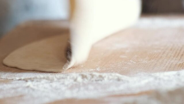 Hands rolling dough balls using rolling pin. Homemade lavash type bread dough is prepared in the village. The camera moves with a panning motion.