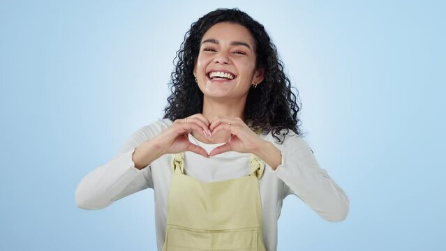 Heart, hands and face of woman in studio for kindness, happy icon and charity donation on blue background. Portrait, model and smile for love, hope and thank you for support, peace and emoji sign