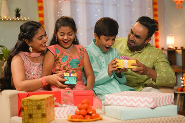 Joyful Indian parents giving diwali surprise gifts to sibling Kids at home - concept of festival celebration, traditional custom or culture and Family Happiness