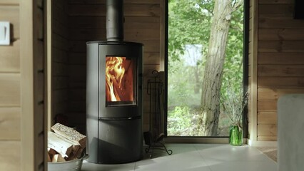 Cozy house chimney fire place fire burning in a tiny house, wooden wall on the background and beautiful window view to the green forest at summer, slow motion.