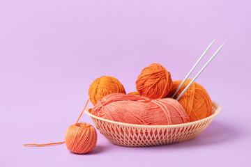 Orange and pink knitting balls in a basket with knitting needles on lilac background. Set for the...
