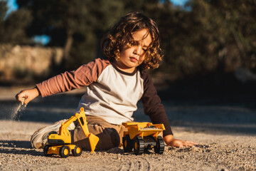 Nice happy little boy playing with excavator machine and truck under sunlight