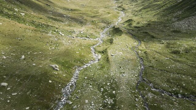 Scenic aerial view of a rocky river in summer pastures with clouds shadows around Val Loga - Italian Alps