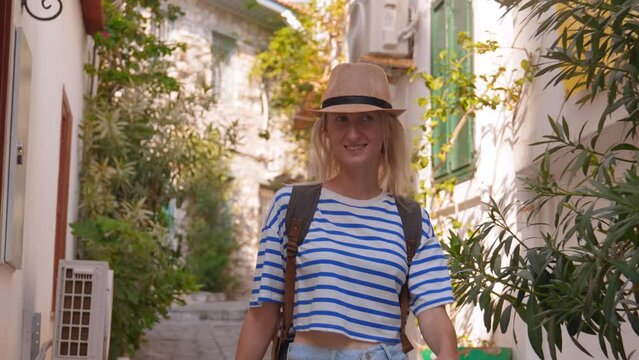 Portrait of young beautiful caucasian slender female tourist with backpack in saloon hat walking on street of old city of Turkey or Greece. Wanderlust concept atmospheric epic beautiful moment.