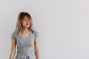 Obraz premium Asian Thai woman wear grey, keep straight face, look inscrutable with messy hair, thinking something while looking at empty space, isolated on white background wall.