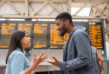 Young couple arguing in front of timetable at a railway station as they missed the train