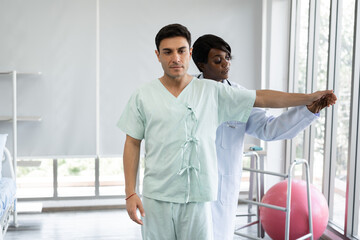 African American Doctor or Physiotherapist working examining treating of caucasian patient, stretching and exercise, in clinic	