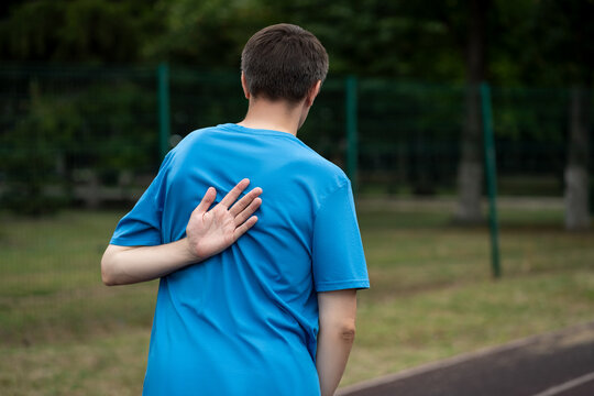 Pain between the shoulder blades, man suffering from backache on a sports ground after workout