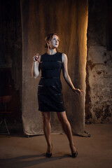Elegant blonde in a medium-length dress. photo in dark colors on a textured wall, warm light