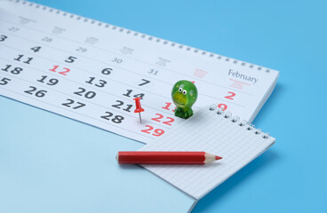 Calendar with marking in red pin of 29 february date. February month calendar, toy frog, notebook and pencil close up on blue background. template fir design - obrazy, fototapety, plakaty