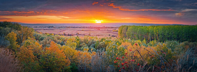 Autumn evening over the valley. Beautiful fall panorama with the multicolored forest and orange october sunset