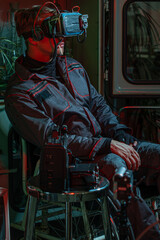 A man in overalls with a cyber helmet on his head, sitting in a wheelchair among old things, high technology and low standard of living of society, concept