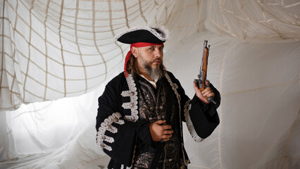 Pirate captain in an embroidered doublet and cocked hat with an antique pistol in his hand,...