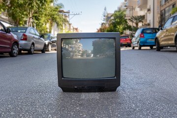 Old plastic black TV set stands on the asphalt of the city street with cars in summer